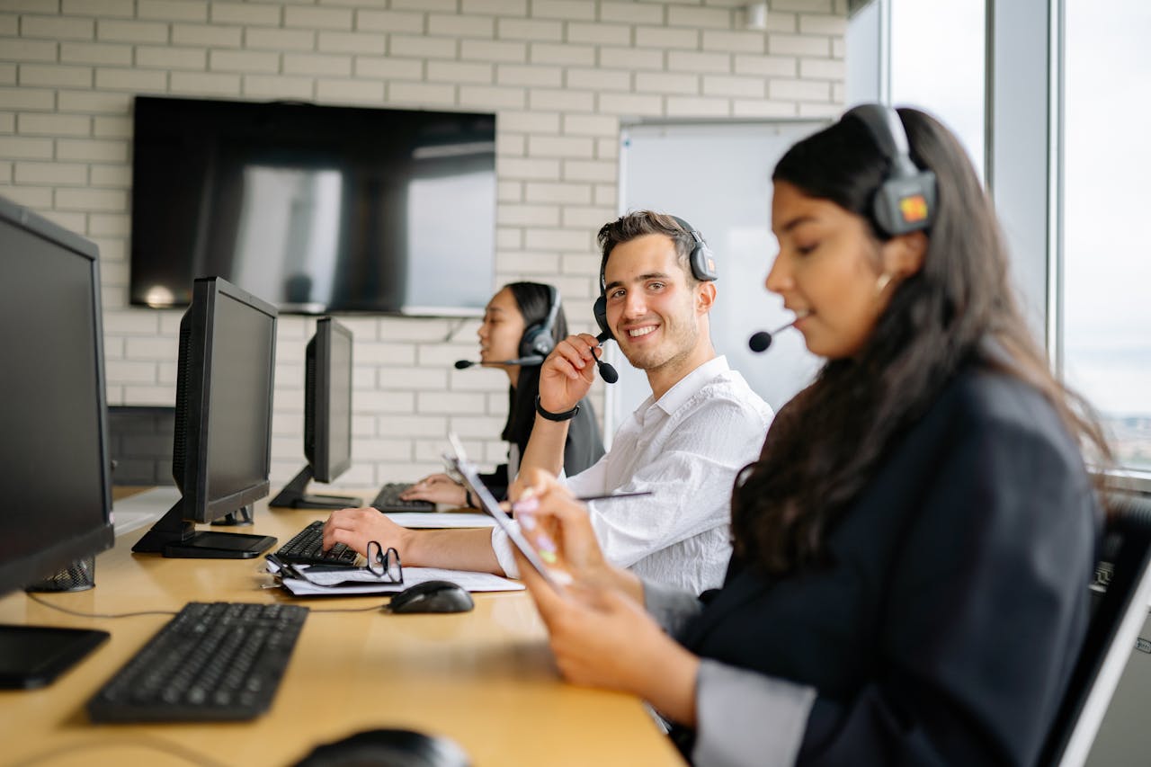 Smiling call center agents wearing headsets, working together in a modern office setting.